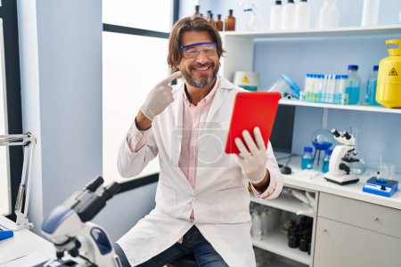 Téléchargez les photos : Bel homme d'âge moyen travaillant au laboratoire scientifique faire appel vidéo sourire heureux pointant avec la main et le doigt - en image libre de droit