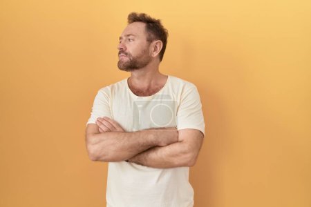Téléchargez les photos : Middle age man with beard standing over yellow background looking to the side with arms crossed convinced and confident - en image libre de droit