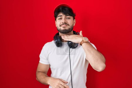 Foto de Hispanic man with beard wearing gamer hat and headphones cutting throat with hand as knife, threaten aggression with furious violence - Imagen libre de derechos