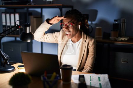 Téléchargez les photos : Belle femme noire travaillant au bureau la nuit très heureuse et souriante regardant loin avec la main au-dessus de la tête. concept de recherche. - en image libre de droit