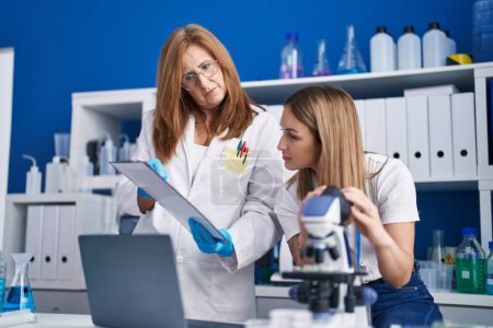 Foto de Científicos de la madre y la hija que escriben en documento usando microscopio en laboratorio - Imagen libre de derechos