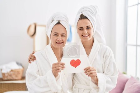 Photo for Middle age woman and daughter wearing bath robe holding heart card winking looking at the camera with sexy expression, cheerful and happy face. - Royalty Free Image