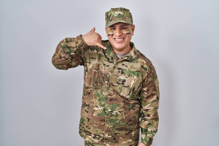 Photo for Hispanic young man wearing camouflage army uniform smiling doing phone gesture with hand and fingers like talking on the telephone. communicating concepts. - Royalty Free Image