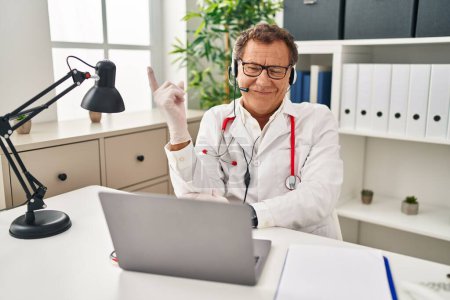 Photo for Senior doctor man working on online appointment with a big smile on face, pointing with hand finger to the side looking at the camera. - Royalty Free Image