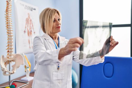 Foto de Mujer rubia de mediana edad que usa uniforme de fisioterapeuta con rayos X en la clínica de fisioterapia - Imagen libre de derechos