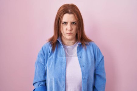 Photo for Young hispanic woman with red hair standing over pink background skeptic and nervous, frowning upset because of problem. negative person. - Royalty Free Image