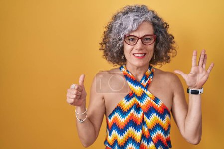 Foto de Middle age woman with grey hair standing over yellow background showing and pointing up with fingers number six while smiling confident and happy. - Imagen libre de derechos