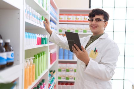 Photo for Non binary man pharmacist using touchpad holding product of shelving at pharmacy - Royalty Free Image
