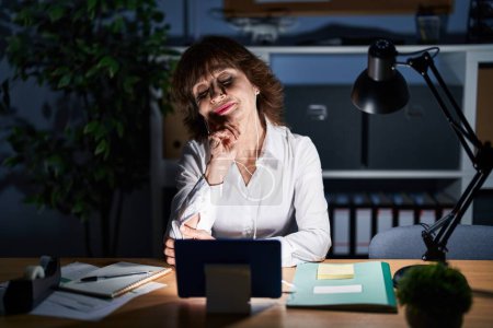 Photo for Middle age woman working at the office at night thinking concentrated about doubt with finger on chin and looking up wondering - Royalty Free Image