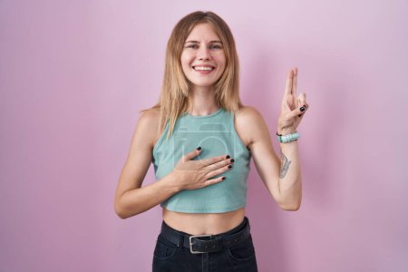 Téléchargez les photos : Blonde caucasian woman standing over pink background smiling swearing with hand on chest and fingers up, making a loyalty promise oath - en image libre de droit
