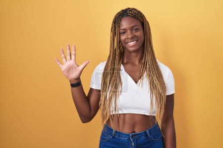 Photo for African american woman with braided hair standing over yellow background showing and pointing up with fingers number five while smiling confident and happy. - Royalty Free Image