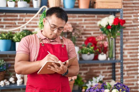 Photo for Young chinese man florist writing on notebook at florist - Royalty Free Image
