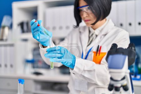 Téléchargez les photos : Young chinese woman scientist pouring liquid on test tube at laboratory - en image libre de droit