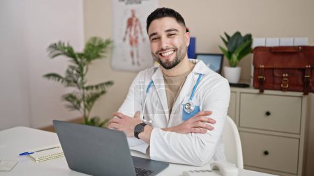 Téléchargez les photos : Jeune homme arabe médecin en utilisant un ordinateur portable travaillant à la clinique - en image libre de droit