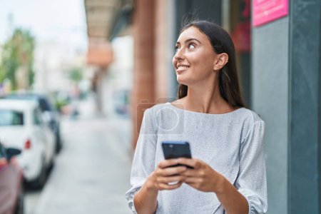 Foto de Joven hermosa mujer hispana sonriendo confiada usando teléfono inteligente en la calle - Imagen libre de derechos