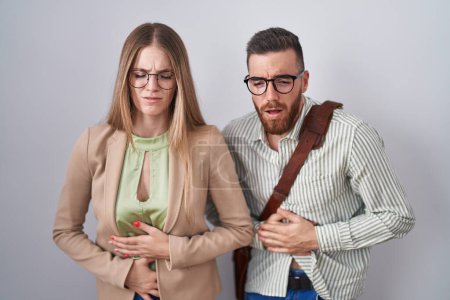 Photo for Young couple standing over white background with hand on stomach because indigestion, painful illness feeling unwell. ache concept. - Royalty Free Image