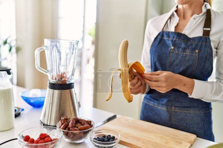 Téléchargez les photos : Jeune femme blonde pelant la banane à la cuisine - en image libre de droit