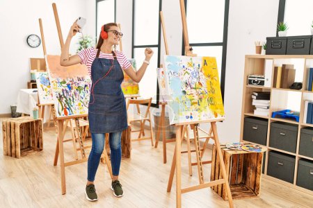Téléchargez les photos : Jeune femme souriante confiante écoutant de la musique et dansant au studio d'art - en image libre de droit