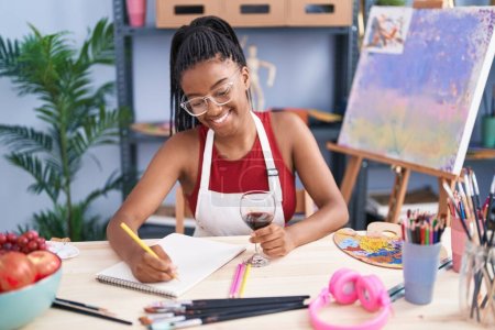 African american woman artist drinking wine drawing on notebook at art studio