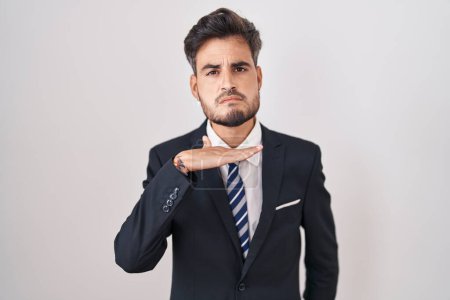 Téléchargez les photos : Jeune homme hispanique avec des tatouages portant un costume d'affaires et une cravate tranchant la gorge avec la main comme un couteau, menace d'agression avec une violence furieuse - en image libre de droit
