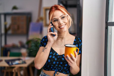 Téléchargez les photos : Jeune artiste femme caucasienne parlant sur smartphone boire du café au studio d'art - en image libre de droit
