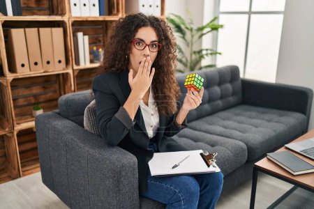 Téléchargez les photos : Jeune femme hispanique jouant jeu d'intelligence cube puzzle coloré couvrant la bouche avec la main, choqué et peur de l'erreur. expression surprise - en image libre de droit