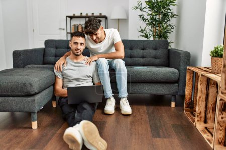 Foto de Dos hombres hispanos en pareja usando laptop abrazándose en casa - Imagen libre de derechos