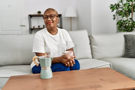Foto de Mujer afroamericana mayor sonriendo confiada bebiendo café en casa - Imagen libre de derechos