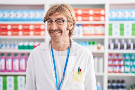 Téléchargez les photos : Homme caucasien avec moustache travaillant à la pharmacie pharmacie souriant regardant vers le côté et regardant loin en pensant. - en image libre de droit