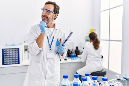 Photo for Middle age man working at scientist laboratory serious face thinking about question with hand on chin, thoughtful about confusing idea - Royalty Free Image