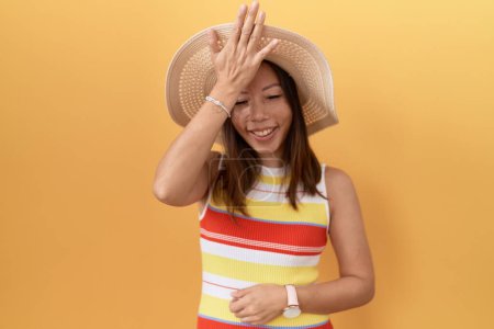 Téléchargez les photos : Femme chinoise du Moyen Age portant chapeau d'été sur fond jaune surpris avec la main sur la tête pour erreur, rappelez-vous erreur. oublié, mauvais concept de mémoire. - en image libre de droit
