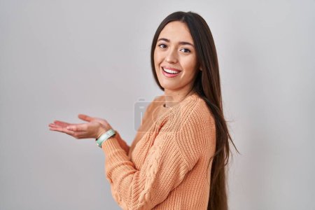 Photo for Young brunette woman standing over white background pointing aside with hands open palms showing copy space, presenting advertisement smiling excited happy - Royalty Free Image