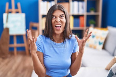 Photo for Brunette young woman sitting on the sofa at home crazy and mad shouting and yelling with aggressive expression and arms raised. frustration concept. - Royalty Free Image
