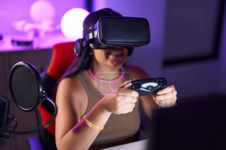 Téléchargez les photos : Jeune belle hispanique femme streamer jouer jeu vidéo en utilisant des lunettes de réalité virtuelle et joystick à la salle de jeu - en image libre de droit