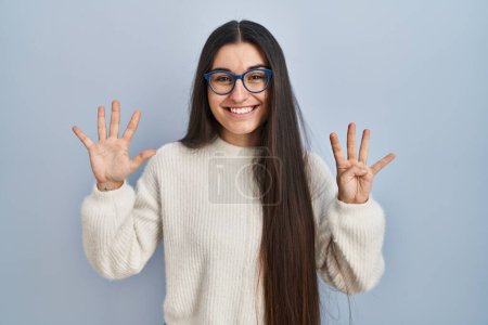 Photo for Young hispanic woman wearing casual sweater over blue background showing and pointing up with fingers number nine while smiling confident and happy. - Royalty Free Image