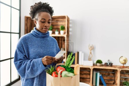 Téléchargez les photos : Femme afro-américaine lisant un reçu alimentaire à la maison - en image libre de droit