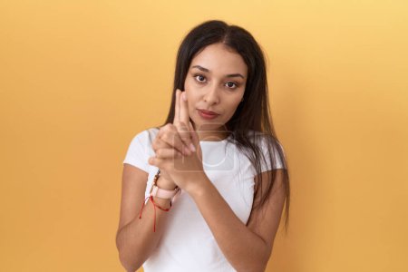 Photo for Young arab woman wearing casual white t shirt over yellow background holding symbolic gun with hand gesture, playing killing shooting weapons, angry face - Royalty Free Image