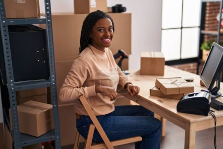 Téléchargez les photos : Jeune afro-américain avec des tresses travaillant dans le commerce électronique des petites entreprises regardant positif et heureux debout et souriant avec un sourire confiant montrant les dents - en image libre de droit