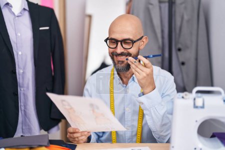 Téléchargez les photos : Young bald man tailor talking on smartphone looking clothing design at tailor shop - en image libre de droit