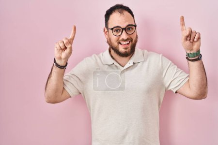 Téléchargez les photos : Plus taille homme hispanique avec barbe debout sur fond rose souriant étonné et surpris et pointant vers le haut avec les doigts et les bras levés. - en image libre de droit