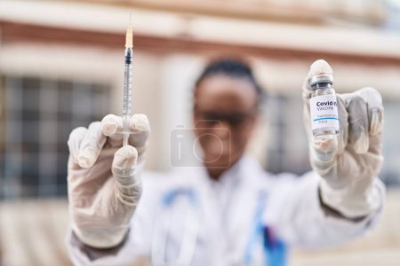 Téléchargez les photos : African american woman doctor smiling confident holding covid-19 vaccine at street - en image libre de droit