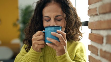 Foto de Mujer hispana de mediana edad bebiendo café de pie en casa - Imagen libre de derechos