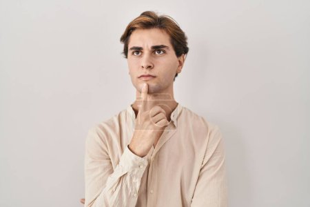 Téléchargez les photos : Jeune homme debout sur fond isolé pensant concentré sur le doute avec le doigt sur le menton et regardant vers le haut se demandant - en image libre de droit