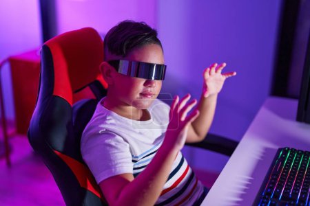 Photo for Adorable hispanic boy streamer playing video game using virtual reality glasses at gaming room - Royalty Free Image