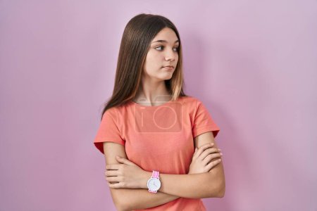 Téléchargez les photos : Adolescente debout sur fond rose regardant du côté avec les bras croisés convaincu et confiant - en image libre de droit