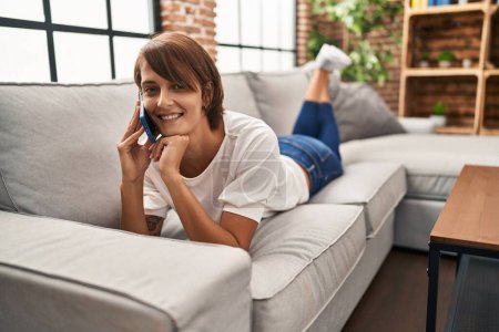 Téléchargez les photos : Jeune belle femme hispanique parlant sur le smartphone couché sur le canapé à la maison - en image libre de droit