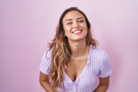 Foto de Mujer hispana joven de pie sobre fondo rosa con las manos juntas y los dedos cruzados sonriendo relajada y alegre. éxito y optimismo - Imagen libre de derechos