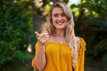 Foto de Mujer joven sonriendo confiada señalando con el dedo en el parque - Imagen libre de derechos