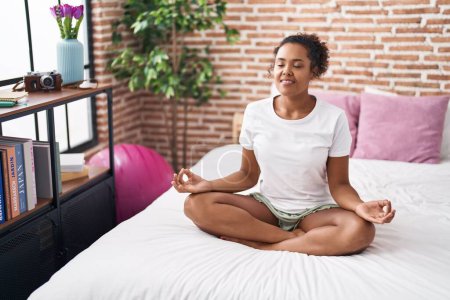 Photo for African american woman doing yoga exercise sitting on bed at bedroom - Royalty Free Image