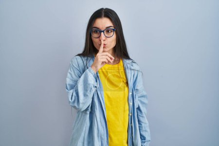 Photo for Young hispanic woman standing over blue background asking to be quiet with finger on lips. silence and secret concept. - Royalty Free Image
